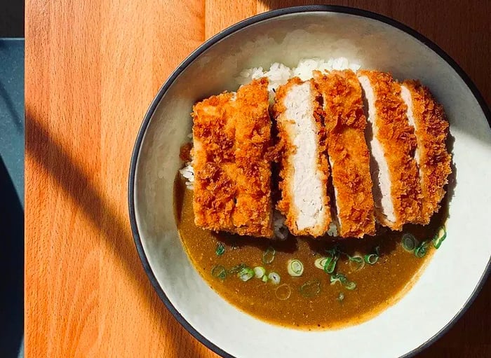 Thick slices of breaded chicken resting in a pool of curry on a white plate.