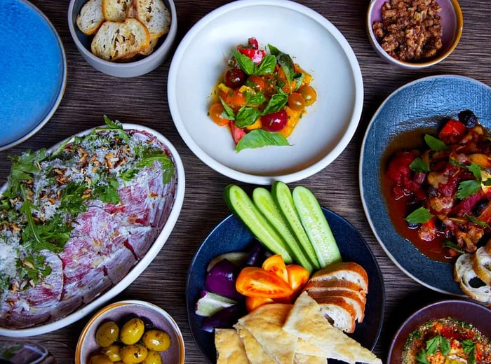 A top-down view of a table adorned with dishes including prosciutto salad, crudités, olives, and nuts.