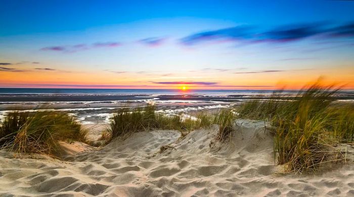 Sand dunes lining a serene lake, illuminated by the sunset.