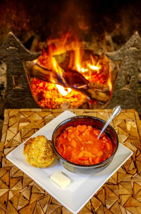 A hearty bowl of bean soup accompanied by a roll and butter, enjoyed in front of a cozy fire.