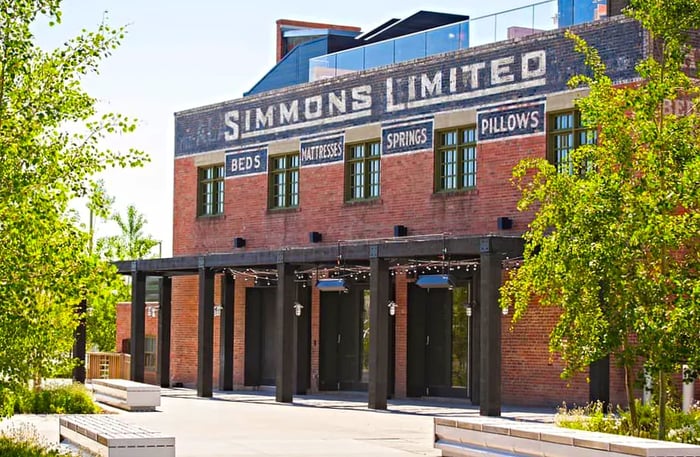 A red brick factory facade marked with the name Simmons Limited, complete with a patio awning adorned with lights out front.