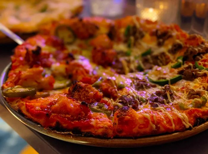 A pizza topped with various meats resting on a metal countertop.