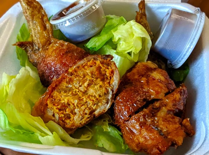 A takeout container holds chicken wings atop a bed of lettuce, accompanied by small cups of sauce.