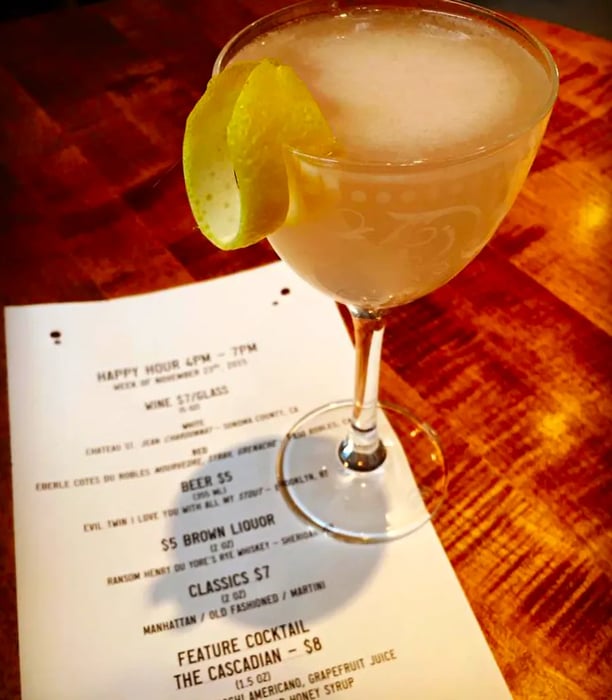 A creamy cocktail served in a nick and nora glass, elegantly garnished with a twist of lemon, resting atop a paper menu.