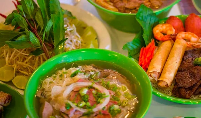 A table laden with a variety of dishes including pho, fresh rolls, and skewered shrimp.