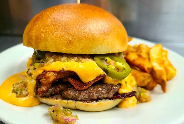 A mouthwatering burger piled high with cheese, jalapeños, and bacon, served alongside thick-cut fries.