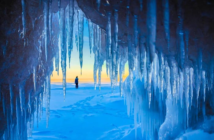 A view from within a cave looking out at a snowy landscape, with icicles adorning the cave's entrance.