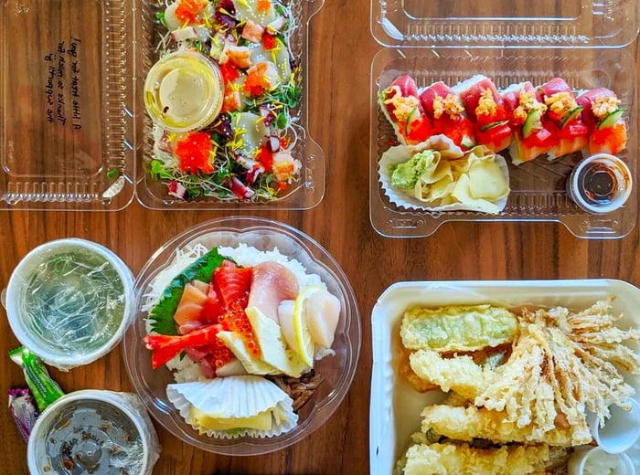 An overhead view of takeout containers brimming with a variety of dishes on a wooden table.