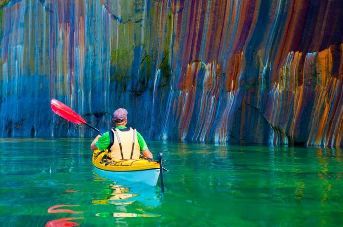 A person kayaking alongside a vibrant cliff face at Pictured Rocks National Lakeshore in Michigan