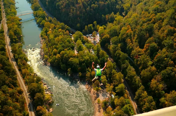 An individual sporting a bright green backpack leaps from the New River Gorge Bridge during the annual Bridge Day celebration in Fayetteville, West Virginia.