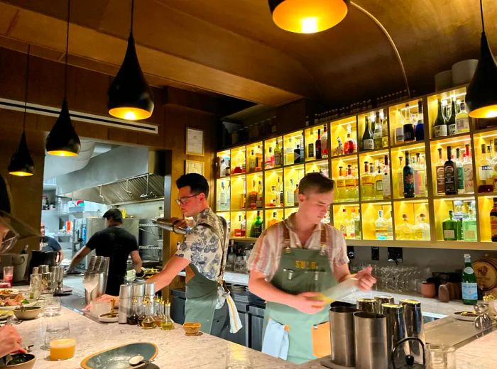 Bartenders serve behind a bar adjacent to the kitchen, with illuminated bottles lining the back wall.