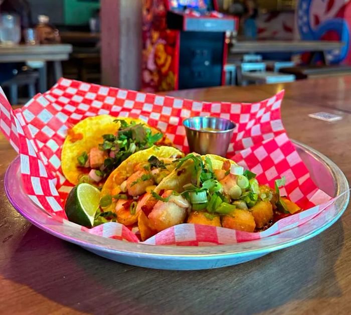 A metal bowl filled with tacos, lined with checkerboard paper.