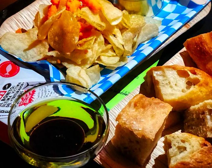 A platter featuring chips, dip, slices of bread, and a glass of wine.