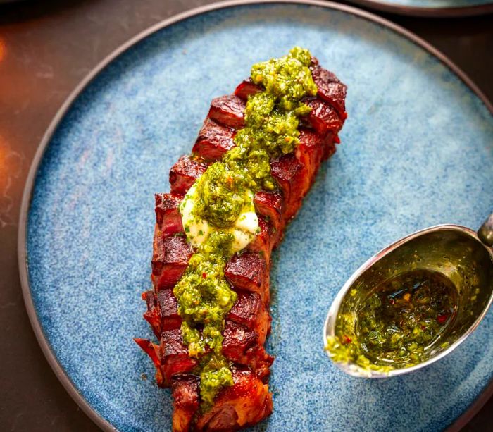 A plated steak garnished with green sauce.