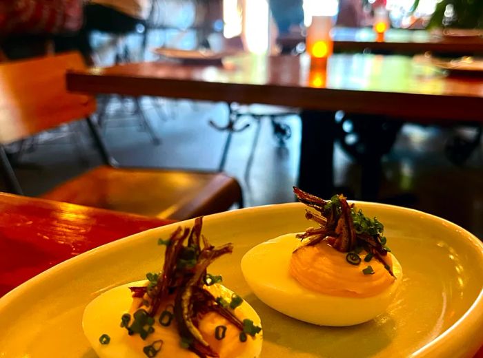 Deviled eggs garnished with anchovies, served in a sunlit dining area where patrons sit at the bar.