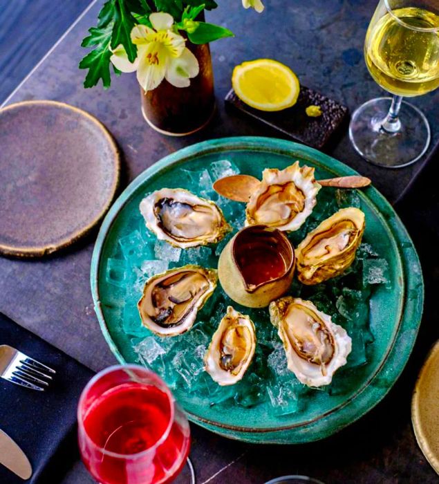 A platter of oysters on ice, accompanied by a sauce for drizzling.