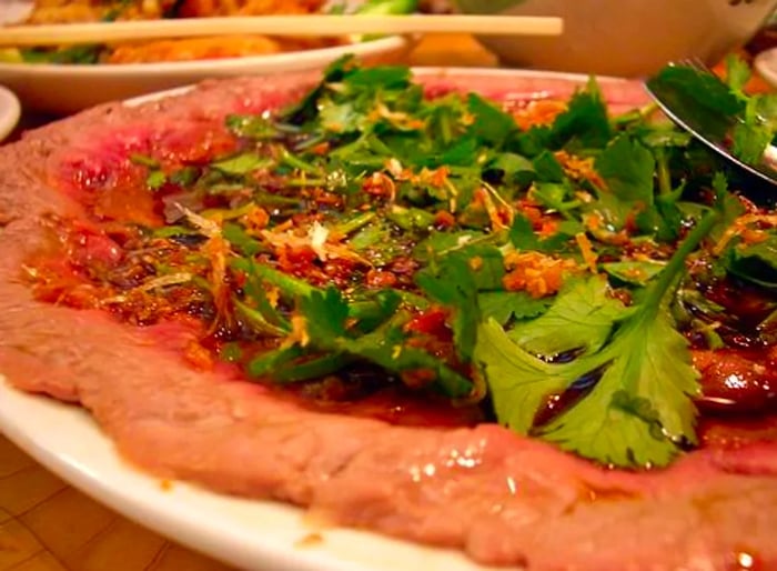 A close-up of a dish featuring a delicate layer of beef in a light sauce, adorned with fresh greens and crunchy garnishes.