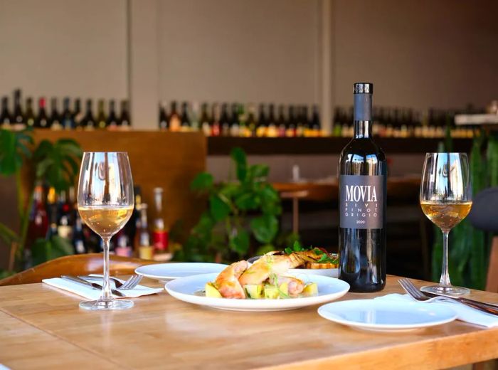 Tables filled with delicious dishes and glasses of wine, set against a backdrop of neatly arranged wine bottles on a shelf.