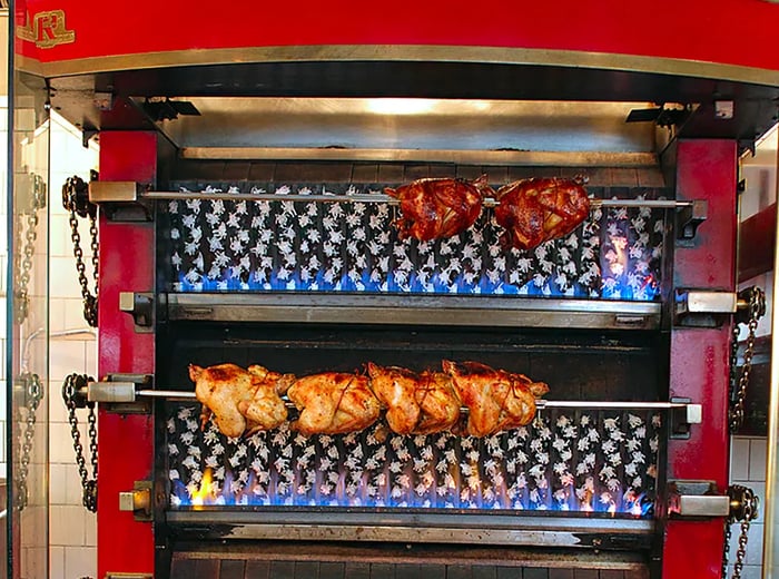 Whole chickens roasting on spits inside a large red rotisserie oven.