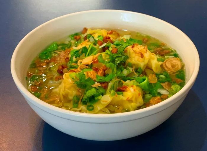 A bowl of soup with wontons and chopped vegetables visible on top