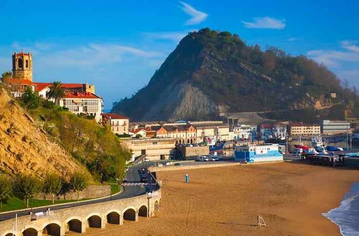 A medieval cityscape along a beach, with a winding road tracing the mountainside