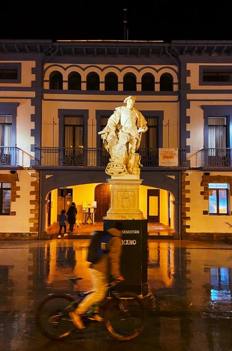 A statue of a sea captain stands in a dimly lit town square