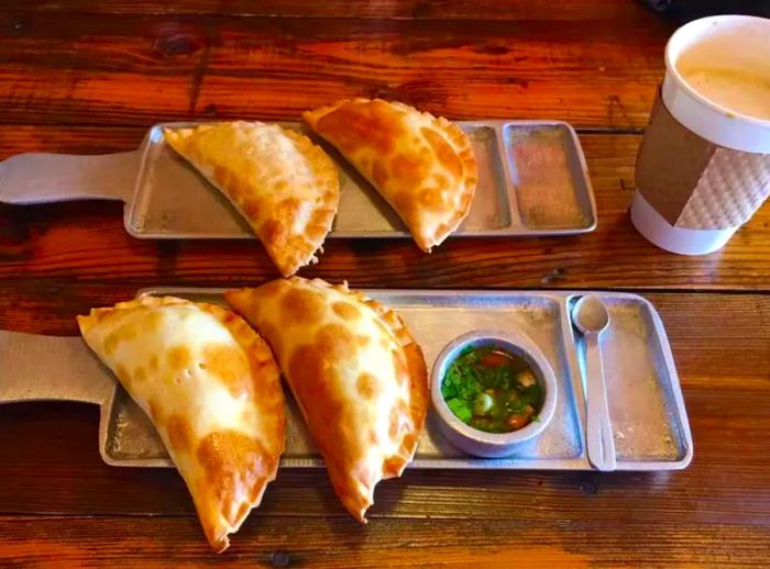 Two trays of empanadas served with dipping sauces and a beverage.