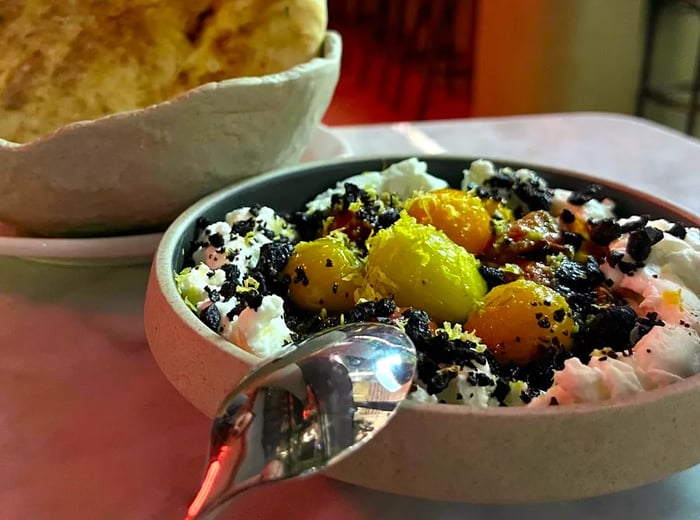 Vibrant chunks of yellow and orange atop creamy white labneh, accompanied by pita.