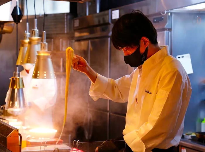 A ramen chef skillfully lifts noodles from a boiling pot under the bright lights of the kitchen.