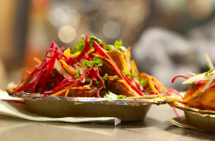 Steam rises from a small tin plate of aloo chaat, captured from the side.