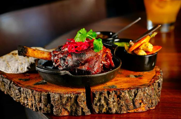 A tender lamb shank rests in a cast iron skillet, adorned with vegetables and cilantro, with additional veggies in small side dishes behind it.