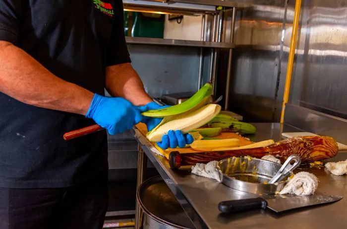 A chef slices a green plantain using a long knife.