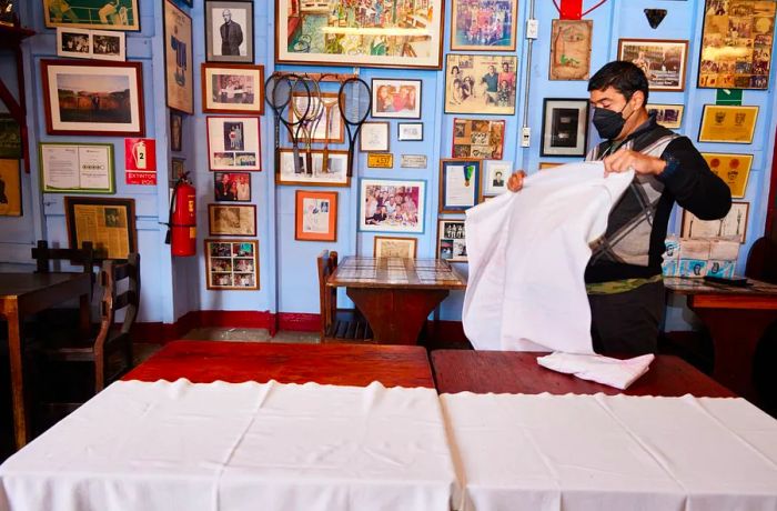 A server shakes out a tablecloth before laying it over a table adorned with vintage images and artifacts.