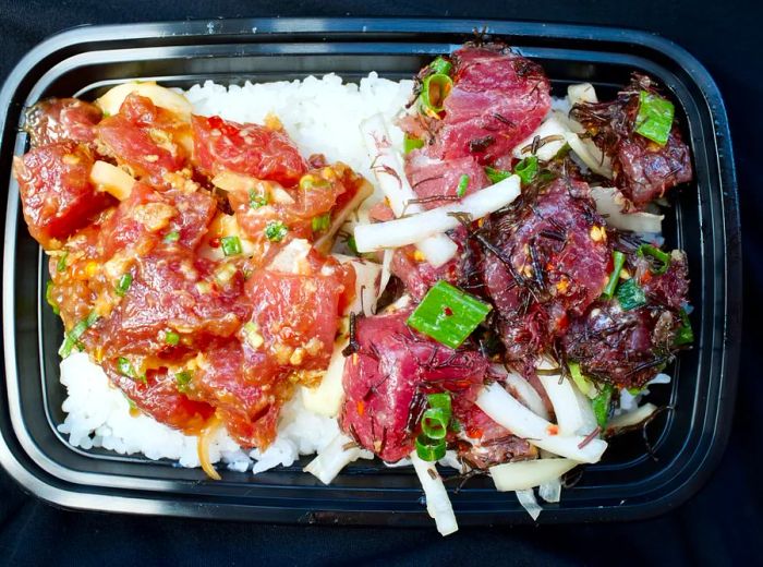 An aerial view of a rectangular takeout container filled with rice and topped with two varieties of ahi poke.