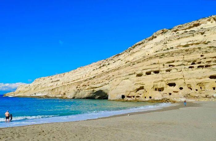 A solitary figure strolls along the deserted beach of Matala, Crete, during winter.