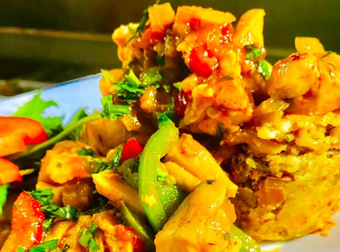 A plate featuring a vibrant seafood medley mixed with cooked chopped vegetables, alongside a towering mound of mofongo in the background.