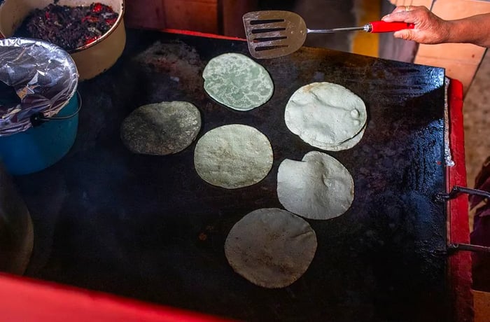 A hand flips tortillas on a comal using a spatula.