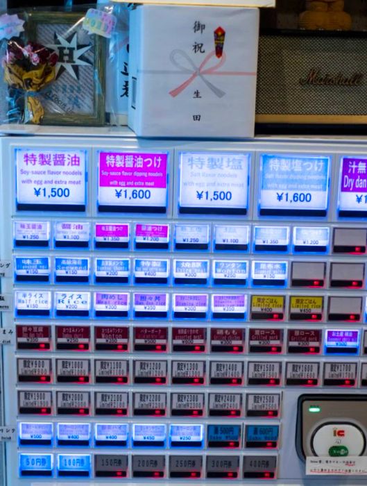 An ordering machine featuring illuminated purple buttons, offering various ramen options displayed in Japanese.