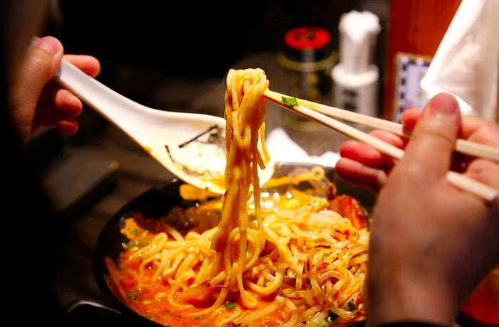 A diner lifts a cluster of ramen noodles using chopsticks.