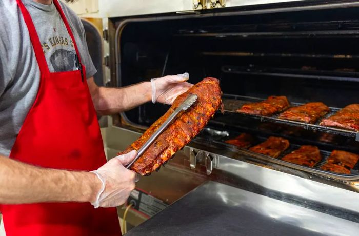 A chef uses tongs to lift a rack of ribs from a smoker.