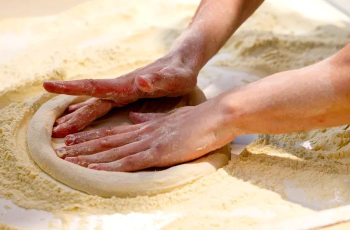 A baker works the dough on a generously floured surface.