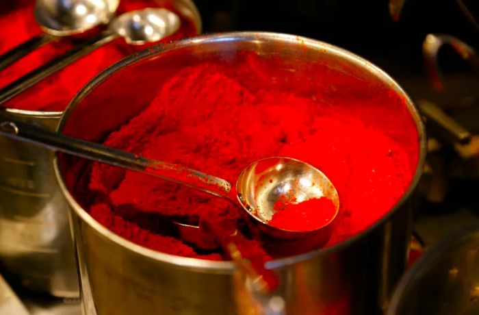 A vibrant bowl filled with bright red spice powder, with a metal spoon resting inside.