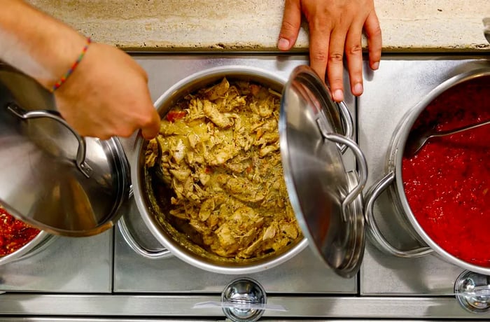 A worker ladles saucy chicken filling from a pot.