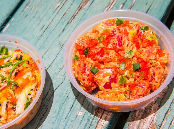 Containers filled with vibrant orange poke on a picnic table.