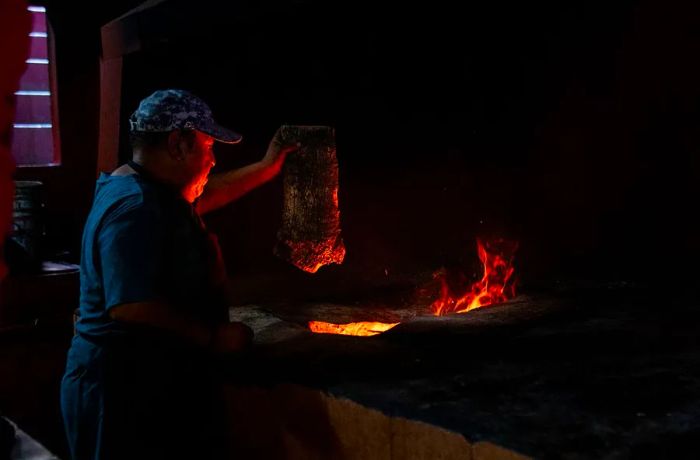 A chef grasps a hefty piece of meat, poised to drop it into a blazing pit.