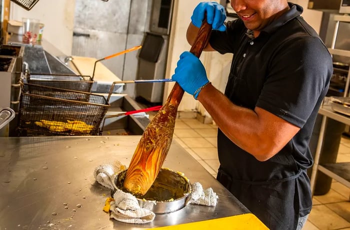 A cook uses a large mortar to mash plantains in a well on the kitchen counter.