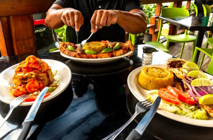 A diner enjoys a pork chop at a table that also features mofongo stuffed with shrimp and a whole fried fish accompanied by plain mofongo.