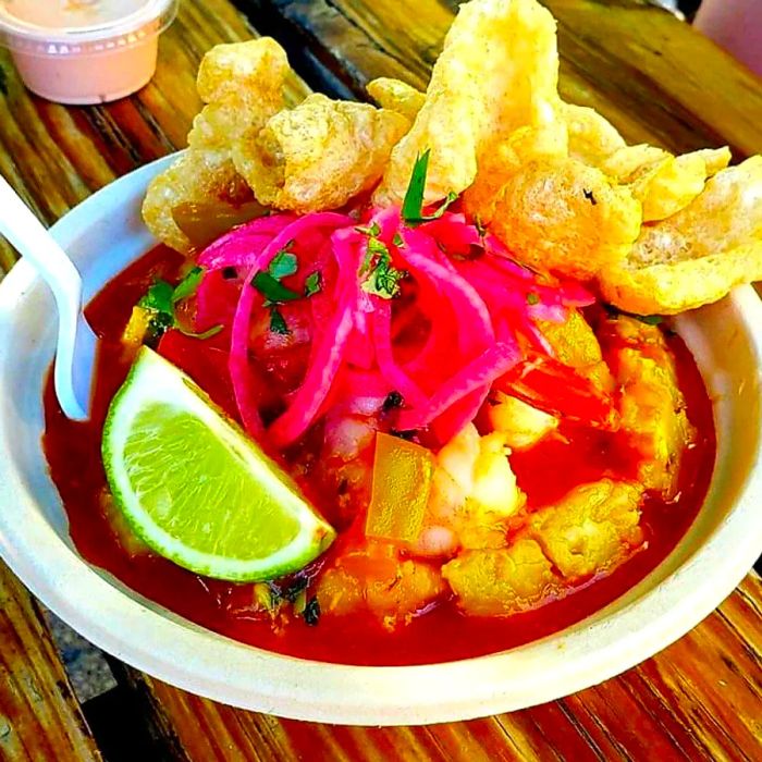 A mofongo topped with sauce, adorned with pickled onions, chicharrones, and a lime wedge.