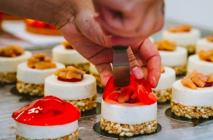 Hands wield an offset spatula to spread a jelly-like topping over a small layered cake.