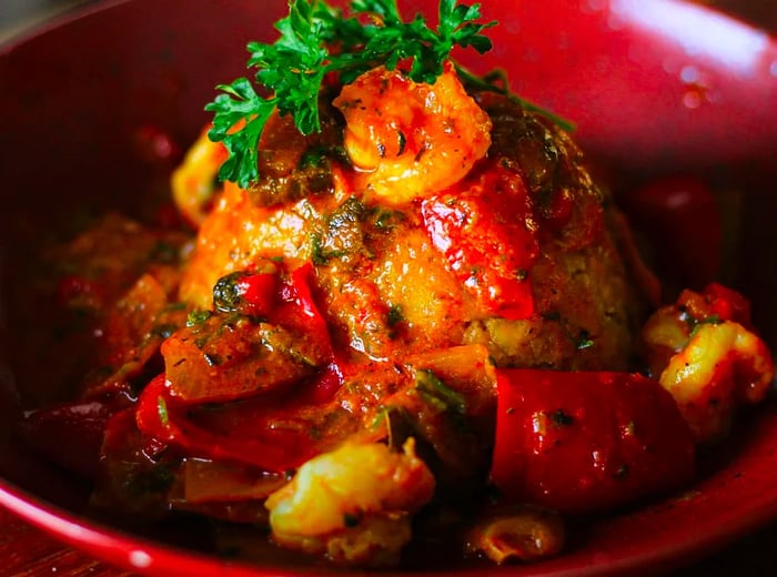 A mofongo draped in sauce, featuring shrimp, tomatoes, and cilantro served in a deep dish.